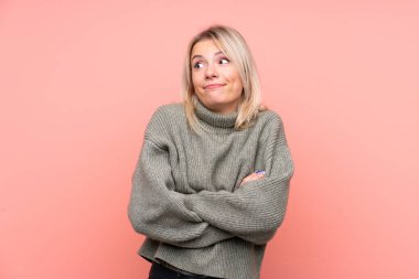 Soyutlanmış pembe arka planda genç sarışın Rus kadın omuzlarını kaldırırken şüpheyle hareket ediyor.