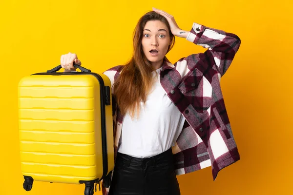 年轻的爱尔兰女人在度假时带着旅行箱 背景是黄色的 感到很惊讶 — 图库照片