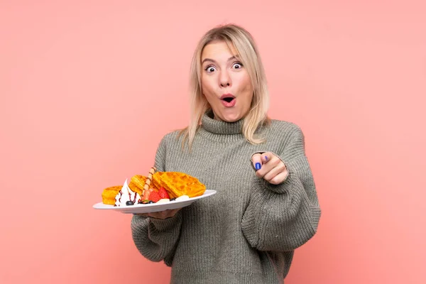 Young Blonde Woman Holding Waffles Isolated Pink Background Surprised Pointing — Stock Photo, Image