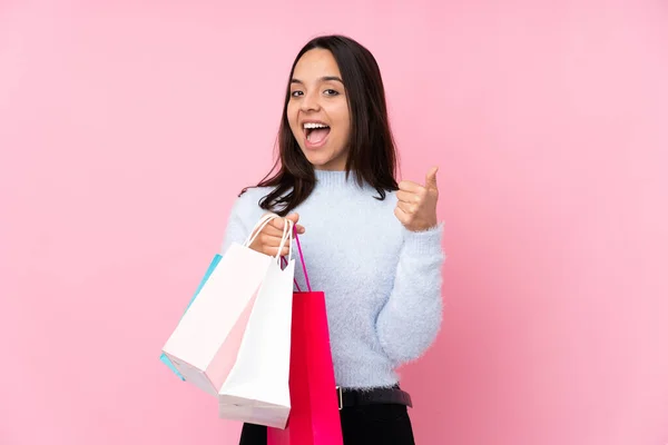 若いです女性とともにショッピングバッグ上の隔離されたピンクの背景ショーOk Signと親指アップジェスチャー — ストック写真