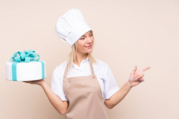 Young Russian woman with a big cake over isolated background pointing to the side to present a product