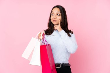 Soyutlanmış pembe arka planda alışveriş çantası taşıyan genç bir kadın yukarı bakarken bir fikir düşünüyor.