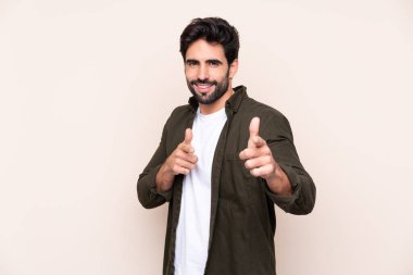 Arka planda sakalları olan genç yakışıklı bir adam ön tarafı işaret ediyor ve gülümsüyor.