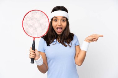İzole edilmiş beyaz arka planda genç bir badmintoncu kadın şaşırdı ve işaret etti.