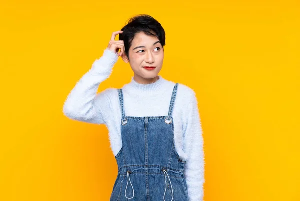Junges Asiatisches Mädchen Overalls Über Isoliertem Gelben Hintergrund Mit Zweifeln — Stockfoto