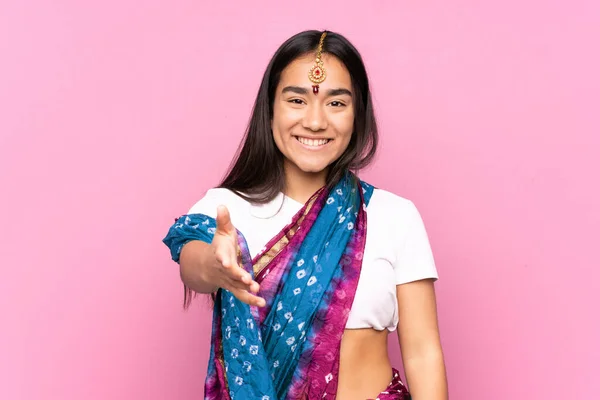 Young Indian woman with sari over isolated background shaking hands for closing a good deal