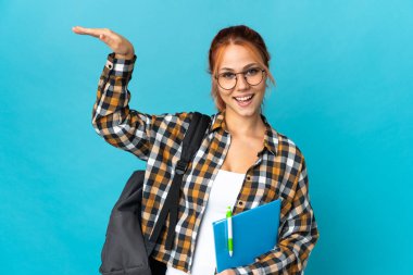 Genç Rus kız öğrenci mavi arka planda izole edilmiş bir ilan vermek için kopyalama alanı tutuyor.