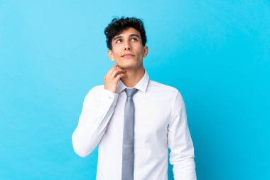 Genç Arjantinli iş adamı mavi arka planda bir fikir düşünüyor.