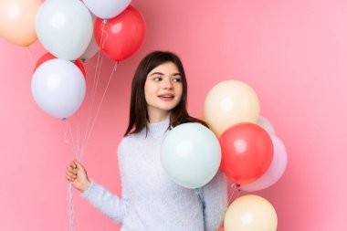 Genç Ukraynalı kız pembe arka planda bir sürü balon tutuyor.