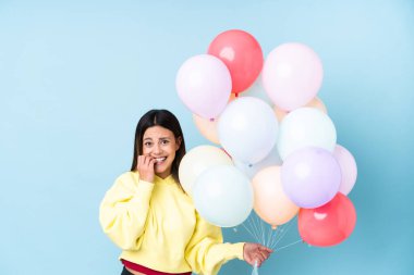 İzole edilmiş mavi arka planda balon tutan kadın gergin ve korkmuş.