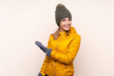 Kış şapkalı kadın izole edilmiş arka planda. Davet edilmek için ellerini yana uzatıyor.