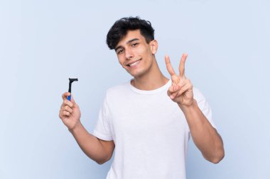 Sakalını kesen beyaz arka planda gülümseyen ve zafer işareti gösteren bir adam.