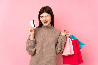 Genç Ukraynalı izole pembe arka planda genç bir kız elinde alışveriş çantaları ve bir kredi kartı tutuyor.