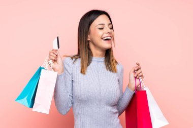 Soyutlanmış pembe arka planda bir kadın alışveriş torbası ve kredi kartı tutuyor.