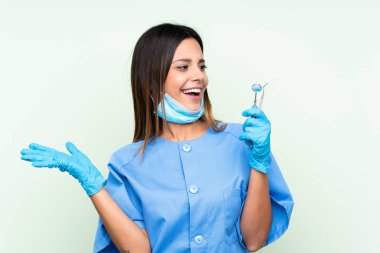 İzole edilmiş yeşil arka planda elinde aletleri tutan kadın diş hekimi.