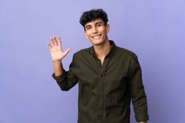 Arjantinli genç adam arka planda izole edilmiş, mutlu bir ifadeyle selamlıyor.