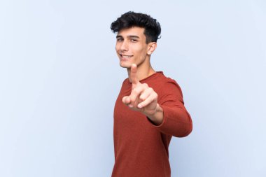 Arjantinli genç adam izole edilmiş mavi arka planda parmağını kaldırıyor ve gösteriyor.