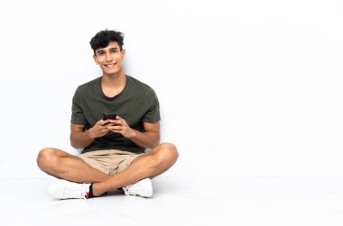 Yerde oturan genç Arjantinli adam cep telefonuyla mesaj yolluyor.