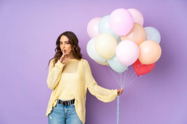 Mor arka planda izole edilmiş balonları yakalayan genç bir kadın sessizlik jesti yapıyor.