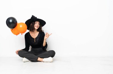 Elinde siyah ve turuncu hava balonları olan genç cadı parmak kaldırarak çözümü anlamaya çalışıyor.