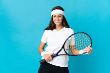 İzole edilmiş mavi arka planda tenis oynayan genç İspanyol kadın.