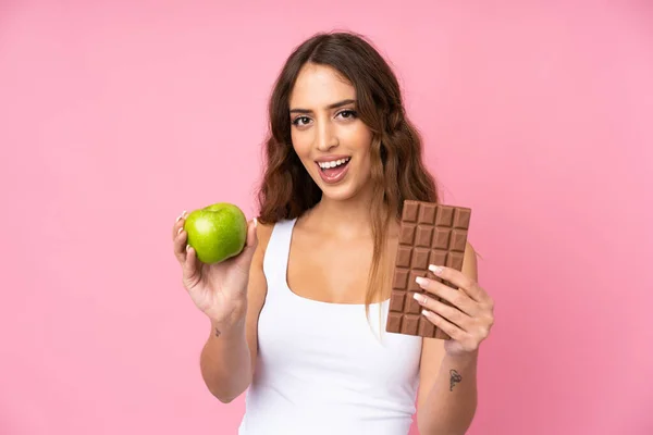 Mladá Žena Izolovaném Růžovém Pozadí Čokoládovou Tabletu Jedné Ruce Jablko — Stock fotografie