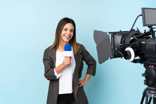 Reporter woman holding a microphone and reporting news over isolated blue background