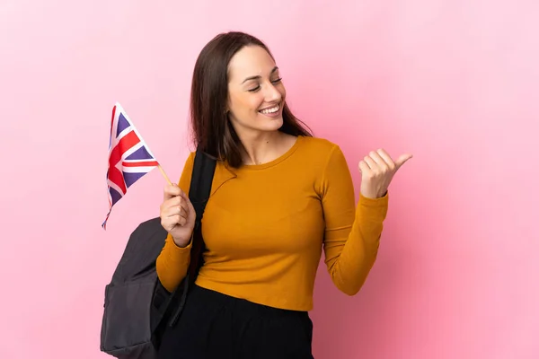 Young hispanic woman holding an United Kingdom flag pointing to the side to present a product