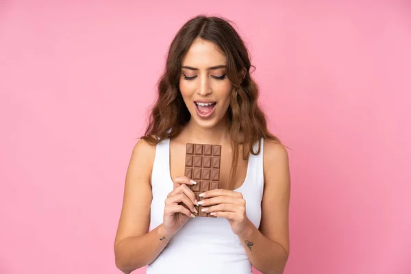 Mladá Žena Nad Izolované Růžové Pozadí Jíst Čokoládové Tablety — Stock fotografie