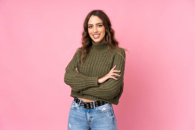Soyutlanmış pembe arka planda genç bir kadın kollarını ön cephede çapraz tutuyor.
