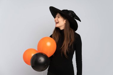 Siyah ve turuncu hava balonları tutan genç cadı yan pozisyonda gülüyor.