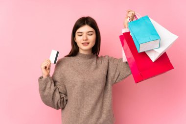 Genç Ukraynalı izole pembe arka planda genç bir kız elinde alışveriş çantaları ve bir kredi kartı tutuyor.