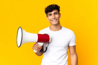 Sarı arka planda izole edilmiş genç Arjantinli bir adam elinde megafonla gülümsüyor.