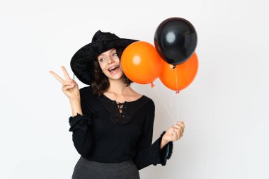 Siyah ve turuncu hava balonları tutan genç cadı gülümsüyor ve zafer işareti gösteriyor.