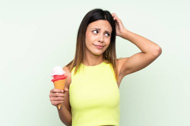 Esmer kadın yeşil arka plan üzerinde kornet dondurma tutuyor. Şüpheleri var ve kafası karışık.