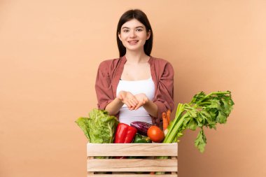 Bir kutuda taze sebze toplayan genç çiftçi kız bir ilan vermek için avuç içinde hayali bir fotokopi makinesi tutuyor.