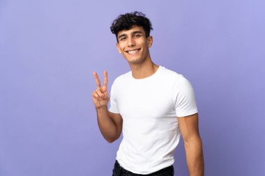 Arjantinli genç adam arka planda izole edilmiş gülümsüyor ve zafer işareti gösteriyor