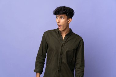 Arjantinli genç adam arka planda izole edilmiş. Yan tarafa bakarken sürpriz jest yapıyor.