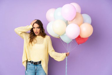 Mor arka planda bir sürü balon yakalayan genç bir kadın. Sürpriz bir yüz ifadesiyle.