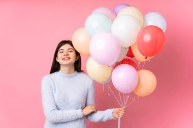 Genç Ukraynalı kız izole edilmiş pembe arka planda bir sürü balon tutuyor ve gülüyor.