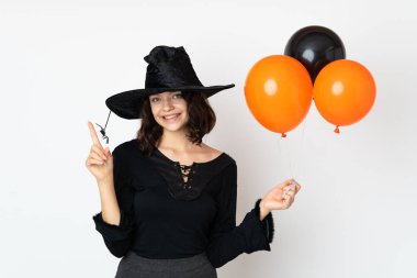 Siyah ve turuncu hava balonları tutan genç cadı en iyinin işareti olarak parmağını kaldırıyor ve gösteriyor.