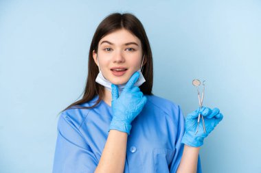Genç dişçi kadın mavi arka planda aletlerle gülüyor.