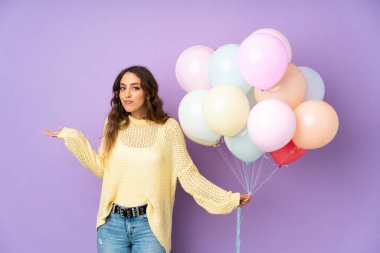 Mor arka planda bir sürü balon yakalayan genç bir kadın, kafa karıştırıcı yüz ifadesiyle ilgili şüpheleri var.