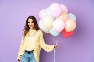 Mor arka planda izole edilmiş balonları yakalayan genç bir kadının şüpheleri ve kafa karıştırıcı bir yüz ifadesi var.