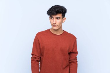 Arjantinli genç bir adam mavi arka planda şüpheli hareketler yapıyor.