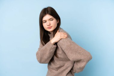 Genç Ukraynalı genç kız, izole edilmiş mavi arka plan üzerine kazak giyerek çabaladığı için omuz ağrısı çekiyor.