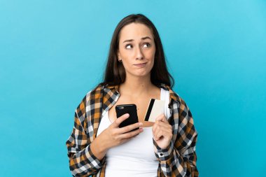 Genç İspanyol bir kadın, mavi arka plandan kredi kartıyla alışveriş yapıyor.