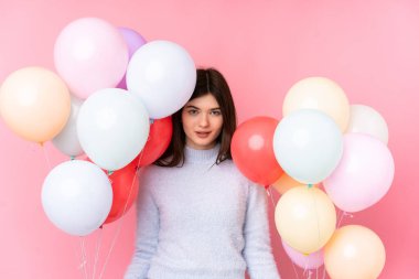 Genç Ukraynalı kız pembe arka planda bir sürü balon tutuyor.