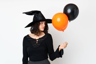 Siyah ve turuncu hava balonları tutan genç cadı yan tarafa bakıyor.