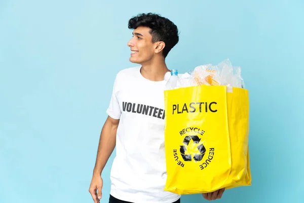 Young Argentinian man holding a bag full of plastic laughing in lateral position